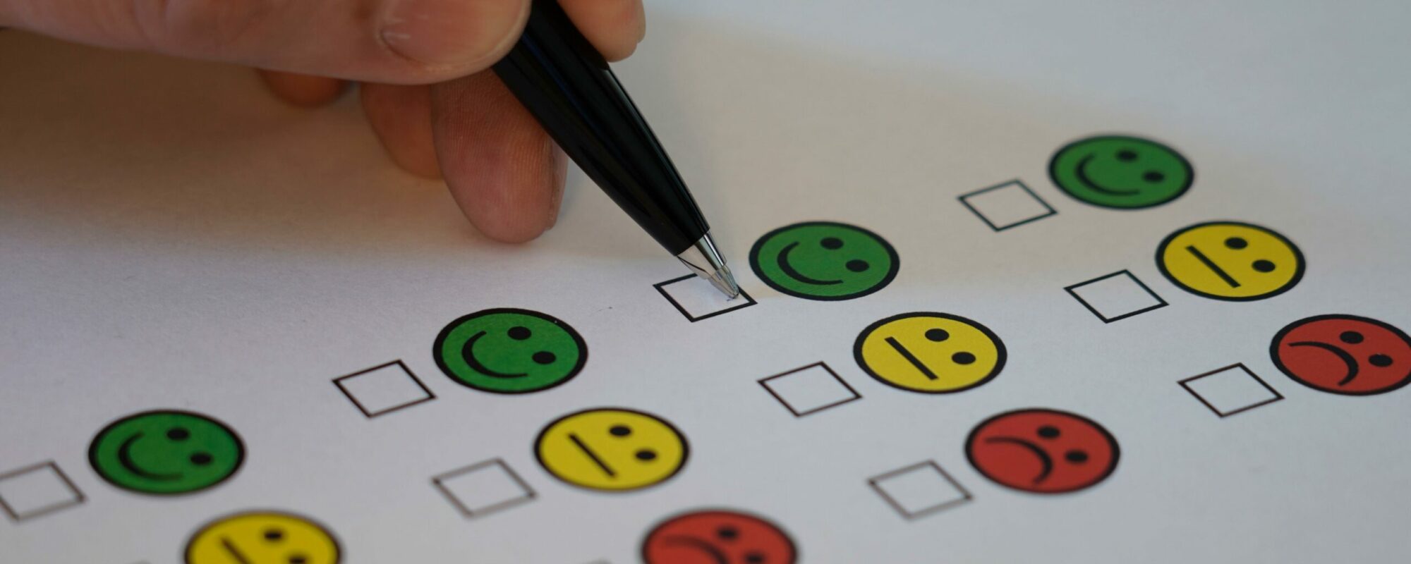 EIn Stift, der eine Umfrage ausfüllt, die mit kleinen Smiley von glücklich bis unglücklich reicht.